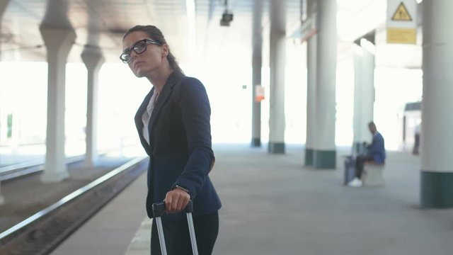 Tired businesswoman with luggage standing at railroad platform and waiting for delayed train