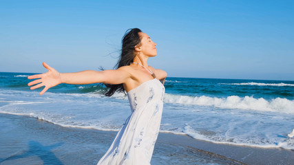 Fototapeta na wymiar Young beautiful woman dressed in a white dress walk barefoot on the summer beach 