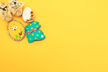 Handmade multi-colored gingerbread cookies in the form of a bunny and Easter eggs, straw shoes and flowers on a yellow background. Gingerbread Easter rabbit, decoration