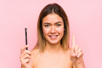 Young caucasian woman holding a eyebrush isolated showing number one with finger.