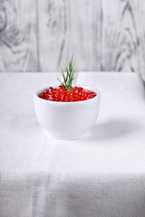 Red caviar in the little ceramic bowl on the edge of the table with white tablecloth