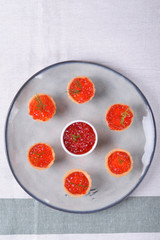 Red caviar served in shortbread tartlets and a ceramic bowl topped with dill on the round plate