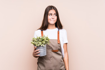 Young gardener caucasian woman holding a plant isolatedconfused, feels doubtful and unsure.