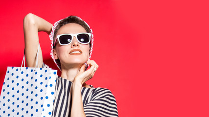 Happy shopping woman with shopping bags over bright red background wearing hat and sunglasses