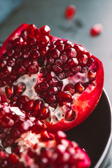 Close up view on a ripe pomegranate in a black plate on a dark background.