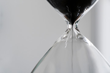 Black sand running through the bulbs of an hourglass measuring the passing time in a countdown to a...