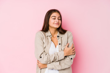 Young caucasian woman posing in a pink background hugs, smiling carefree and happy.