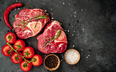 two raw beef steaks with tomatoes and spices on a concrete background with copy space for your text. Concept of cooking dinner for two