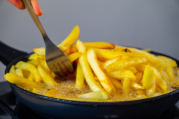 A fork takes the french fries from the black pan