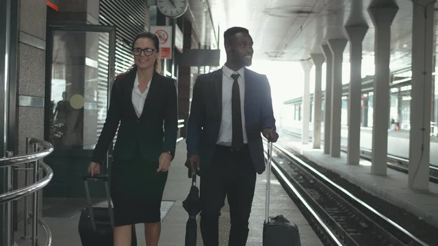 Multiracial business couple walking along train platform waiting for boarding.