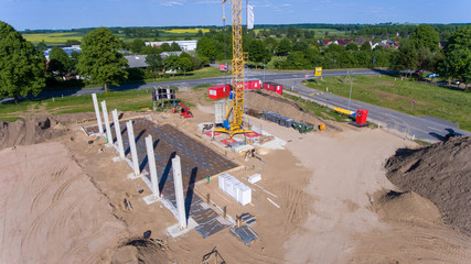 Drone photos of a large construction site on which a factory building is being erected. The foundations for the piers have been laid and and the first piers have been erected