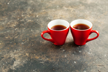 Two red cups of hot espresso are turned to each other on a dark textured surface. Concept of a romantic date for Valentines Day in a cozy place. February 14 greeting card design