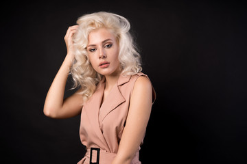Naklejka premium Stylish blonde woman touching hair isolated on black background