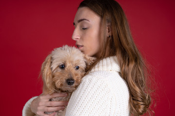 Beautiful woman in sweater holding dog isolated on red background