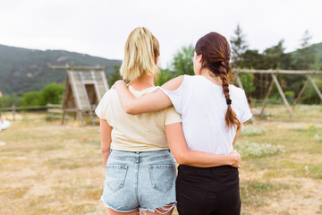 Two young women friends on her back with hair in a braid and blonde hair hugging each other in the countryside. Friendship concept.