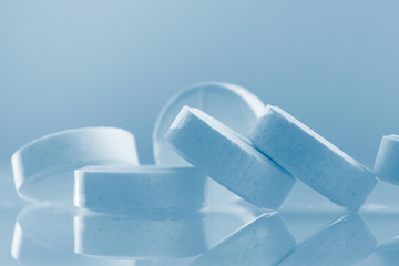 White large round pills with blue tint. Medicines on a glass surface close-up