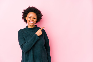 Middle aged african american woman against a pink background isolated smiling and pointing aside, showing something at blank space.