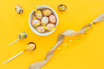 Easter border composition with golden decorated eggs in plate, polka dot ribbon, spoons on yellow backdrop. Stylish decor minimal concept. Copy space. Festive flat lay greeting card