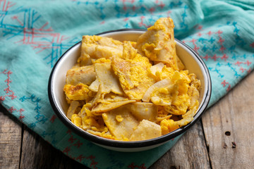 Mexican scrambled eggs with corn tortilla also called migas on wooden background