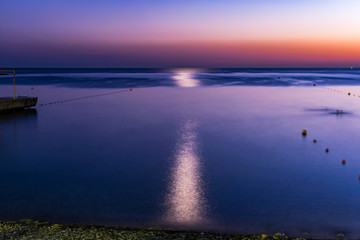 Красивый, красочный и контрастный закат над морем, океаном. Горячее солнце освещает просторный пейзаж, отбрасывая блики лучей на водную гладь. Яркий солнечный восход. Путешествие и туризм.