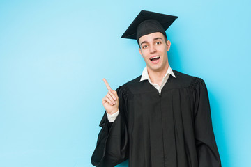 Young caucasian graduated man smiling cheerfully pointing with forefinger away.