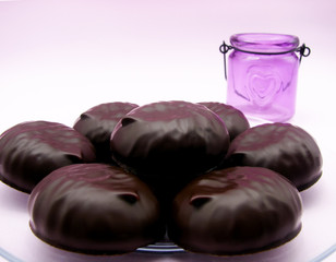 Chocolate-covered marshmallows on a transparent plate, a purple candlestick with a heart  on a pink background. Valentine's Day.