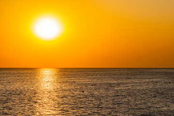 Fototapeta na wymiar Красивый, красочный и контрастный закат над морем, океаном. Горячее солнце освещает просторный пейзаж, отбрасывая блики лучей на водную гладь. Яркий солнечный восход. Путешествие и туризм.