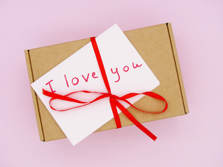 Gift box rewound with a red bow on a pink background. There's a note on the box that says " I love you." Valentine's day. 