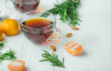 Tea in a glass cup on a light wooden background. Black tea with rosemary and tangerines. Space for text.