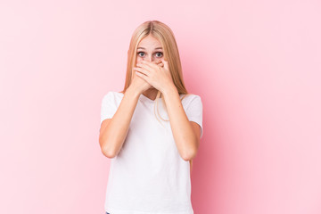 Young blonde woman on pink background shocked covering mouth with hands.
