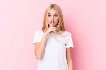 Young blonde woman on pink background keeping a secret or asking for silence.