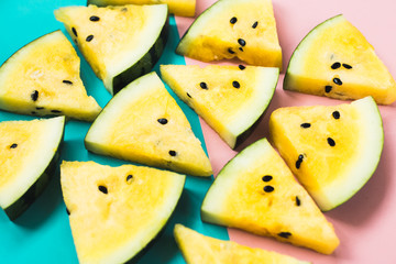cut off triangular slices of ripe yellow watermelon on pink-blue background