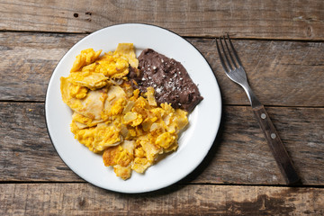Mexican scrambled eggs with corn tortilla also called migas on wooden background