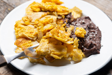 Mexican scrambled eggs with corn tortilla also called migas on wooden background