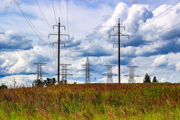 High voltage electric poles in the field on sky with clouds.