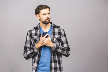 Always in touch. Serious young man holding smart phone and looking at it. Portrait of a happy young man using mobile phone isolated over grey background.