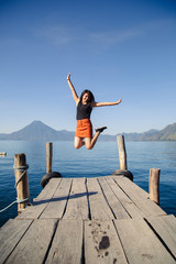 Fototapeta na wymiar Traveling girl jumping on the pier of Lake Atitlan in Guatemala - Young adventurer in Latin American tourist destination - young energetic at sunrise