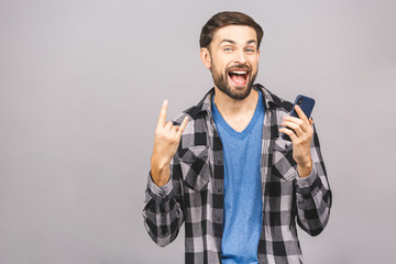 Fototapeta premium Always in touch. Serious young man holding smart phone. Portrait of a happy young man using mobile phone isolated over grey background.