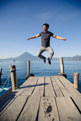 Naklejka na ściany i meble Young traveler jumping on the pier of Lake Atitlan in Guatemala - Young adventurer in Latin American tourist destination- young energetic at sunrise