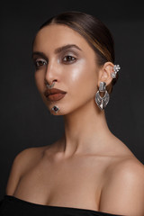 Obraz premium Grace woman in low-cut black dress, make-up, with silver bijouterie, looking at camera, over dark grey background.