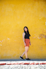 Fototapeta premium Traveling girl in colonial city - Hispanic woman standing in front of yellow old wall - Young woman is posing in the streets of the historical city Guatemala