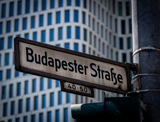A close up photo of a street sign with the German name Budapester Strasse, mounted on a lamp post in the city center called Kurfürstendamm, Berlin, Germany
