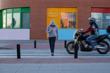 Caucasian boy about to be hit by a motorbike at a pedestrian crossing as he is distractedly looking at his mobile phone. Road safety education and technology.