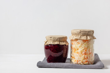 Homemade sauerkraut with carrots and cabbage salad with beets in a glass jar on a white wooden background. Fermented food.