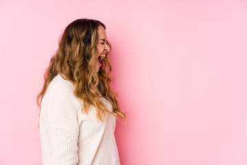 Young curvy woman posing in a pink background isolated shouting towards a copy space