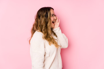 Naklejka premium Young curvy woman posing in a pink background isolated shouting and holding palm near opened mouth.