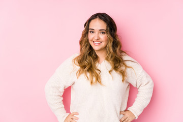 Young curvy woman posing in a pink background isolated confident keeping hands on hips. - obrazy, fototapety, plakaty