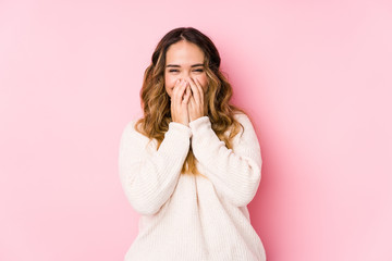 Young curvy woman posing in a pink background isolated laughing about something, covering mouth...