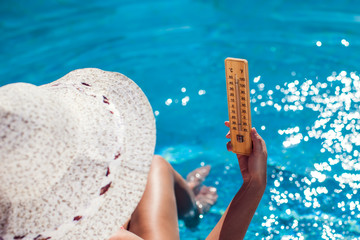 Woman holding thermometer on the pool background. Hot weather and summer concept