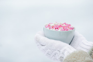 Female hands holdink white cup of coffee with white and pink marshmallows